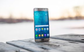 Smartphone Samsung apoiado sobre uma superfície de madeira ao ar livre, durante o pôr do sol.