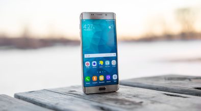 Smartphone Samsung apoiado sobre uma superfície de madeira ao ar livre, durante o pôr do sol.