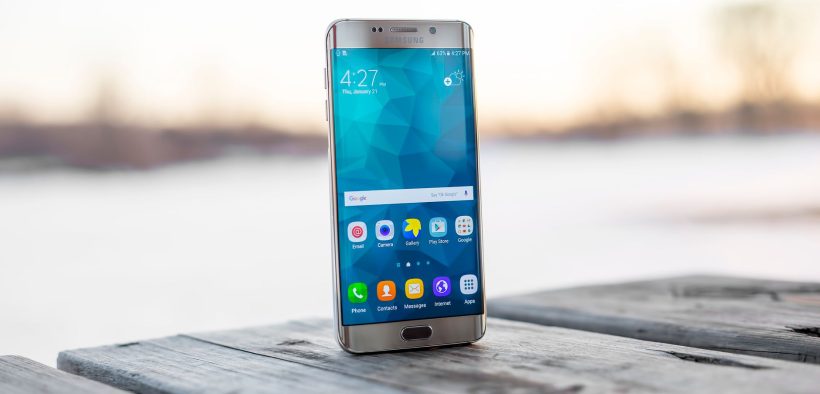 Smartphone Samsung apoiado sobre uma superfície de madeira ao ar livre, durante o pôr do sol.