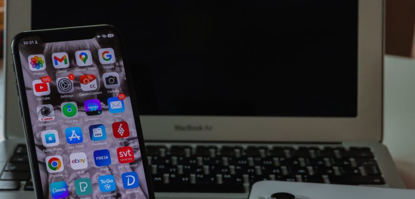 Notebook aberto ao lado de um smartphone sobre uma mesa, representando produtividade e conectividade entre dispositivos.