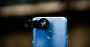 Close de uma lente óptica acoplada à câmera de um smartphone, com fundo desfocado.