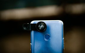 Close de uma lente óptica acoplada à câmera de um smartphone, com fundo desfocado.