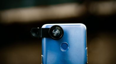 Close de uma lente óptica acoplada à câmera de um smartphone, com fundo desfocado.