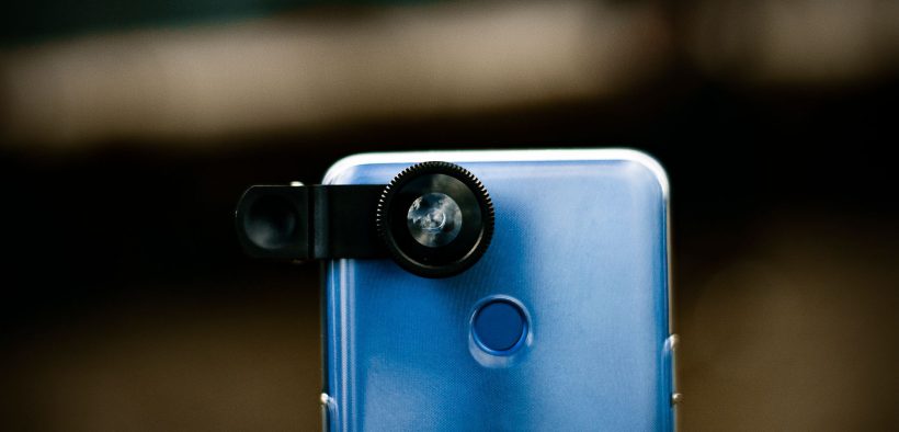 Close de uma lente óptica acoplada à câmera de um smartphone, com fundo desfocado.