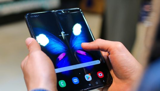 Mãos seguram um smartphone dobrável aberto, com a tela exibindo a imagem de uma borboleta.