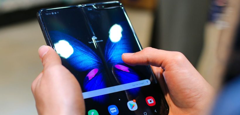 Mãos seguram um smartphone dobrável aberto, com a tela exibindo a imagem de uma borboleta.