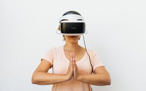 Mulher adulta medita usando um headset de realidade virtual diante de fundo branco.