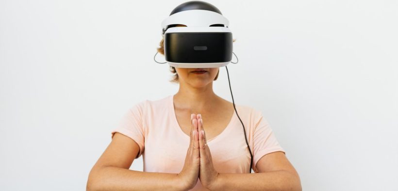 Mulher adulta medita usando um headset de realidade virtual diante de fundo branco.