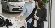 Homem conversa com uma vendedora sobre as características de um veículo híbrido em um showroom de automóveis.