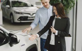 Homem conversa com uma vendedora sobre as características de um veículo híbrido em um showroom de automóveis.