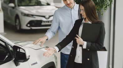 Homem conversa com uma vendedora sobre as características de um veículo híbrido em um showroom de automóveis.