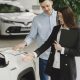Homem conversa com uma vendedora sobre as características de um veículo híbrido em um showroom de automóveis.