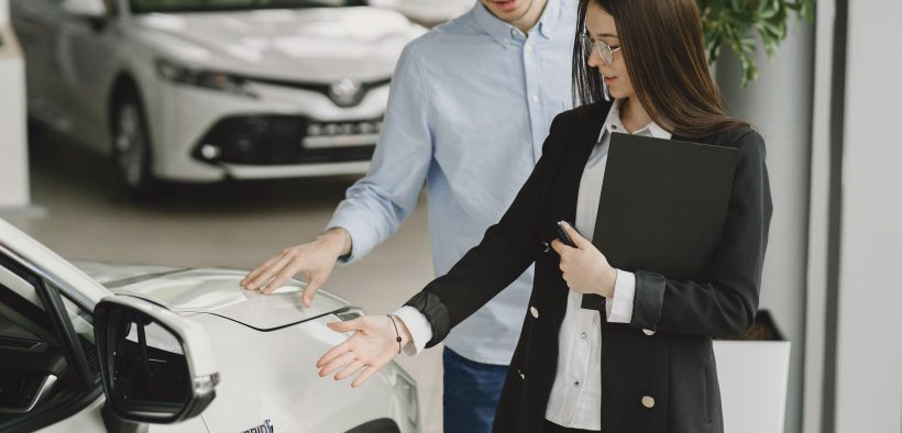 Homem conversa com uma vendedora sobre as características de um veículo híbrido em um showroom de automóveis.