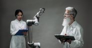 Dois pesquisadores trabalham com um braço robótico em um laboratório de tecnologia.