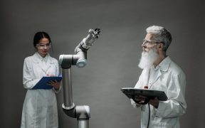 Dois pesquisadores trabalham com um braço robótico em um laboratório de tecnologia.