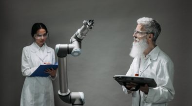 Dois pesquisadores trabalham com um braço robótico em um laboratório de tecnologia.