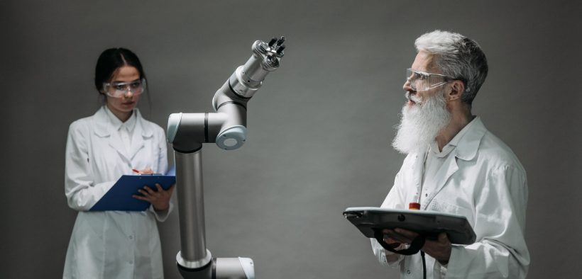 Dois pesquisadores trabalham com um braço robótico em um laboratório de tecnologia.