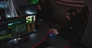 Profissionais de cibersegurança monitoram sistemas de computador em uma sala com iluminação baixa.