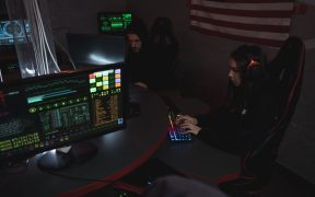 Profissionais de cibersegurança monitoram sistemas de computador em uma sala com iluminação baixa.