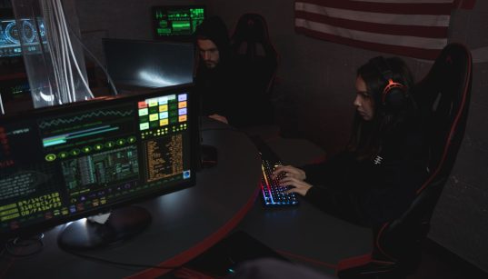 Profissionais de cibersegurança monitoram sistemas de computador em uma sala com iluminação baixa.