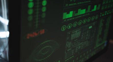 Tela de computador exibindo interfaces digitais de cibersegurança e proteção de dados em tons verdes.