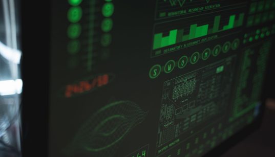 Tela de computador exibindo interfaces digitais de cibersegurança e proteção de dados em tons verdes.